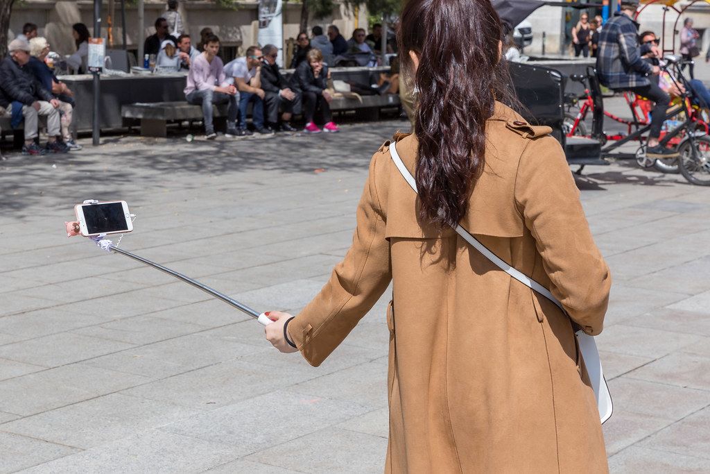Woman takes a selfie with a selfiestick in front of the cathedral at the Placita de La Seu in Barcelona, Spain