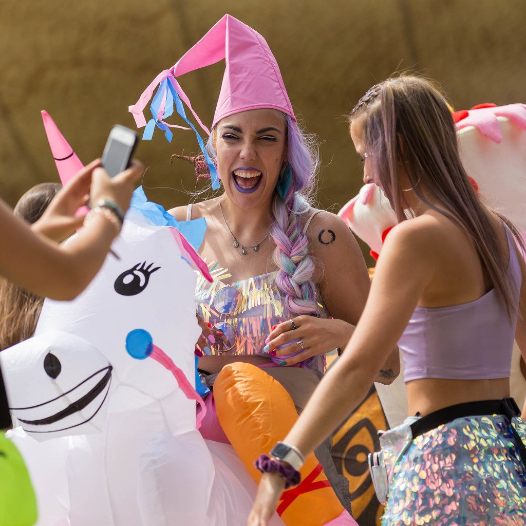 Women with colorful hair laugh and ride on inflatable unicorns at the Tomorrowland Festival