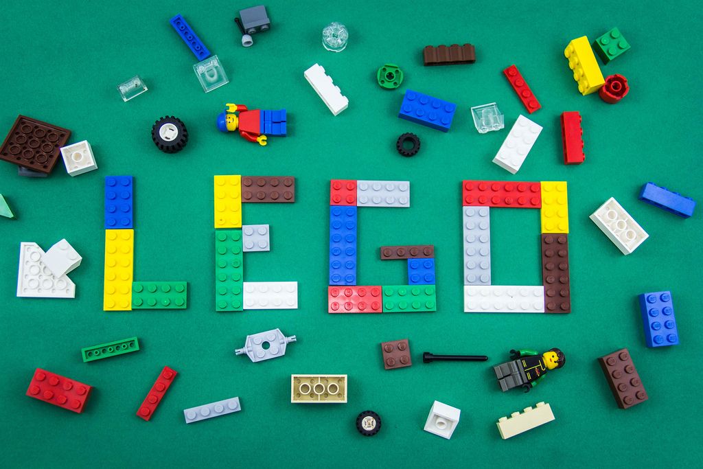 Wort LEGO, gebildet aus Legosteinen zwischen Legofiguren und bunten Legosteinen auf grünem Hintergrund