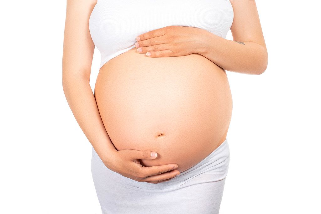 Young pregnant woman waiting for her baby's birth holding her tummy on white background