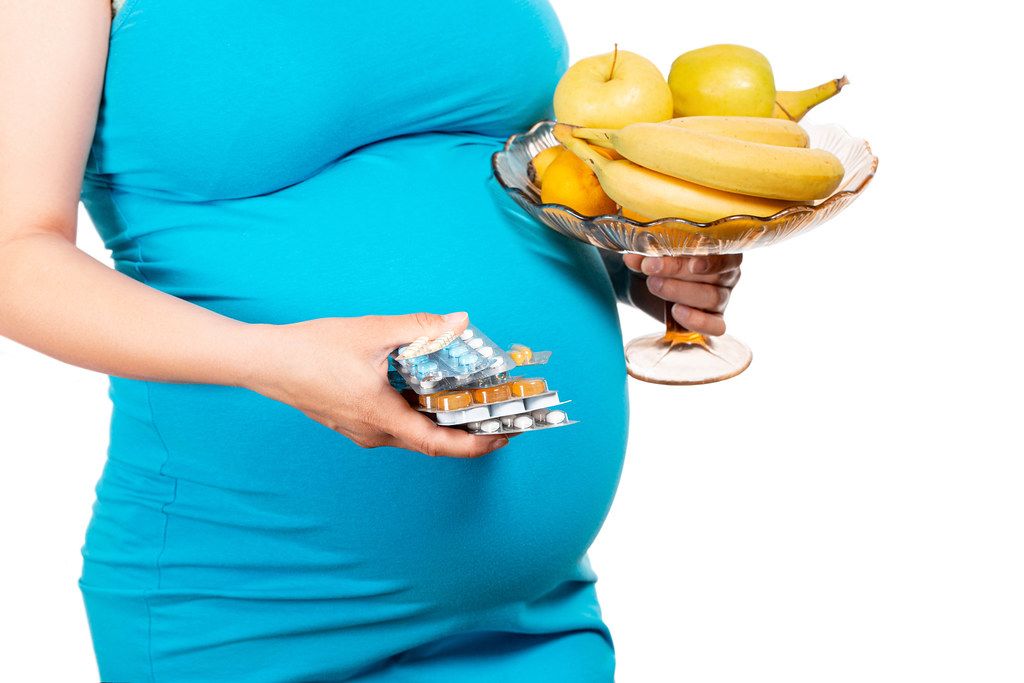 Young woman's holding blister packs of pills and fresh fruits. Concept receiving vitamins in pregnancy time