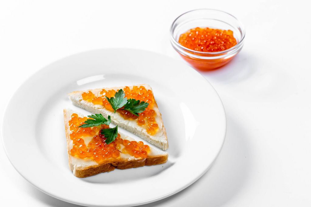 Zwei dreieckige Sandwiche mit gesalzenem rotem Kaviar auf weißem Hintergrund