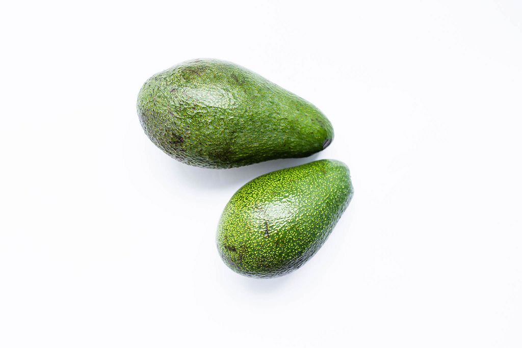 Zwei ganze reife grüne Avocados liegen auf weißem Hintergrund