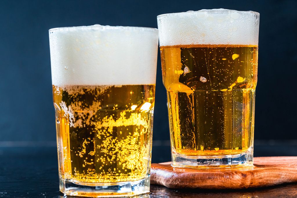 zwei Gläser helles Bier mit Schaumkrone vor dunklem Hintergrund ...
