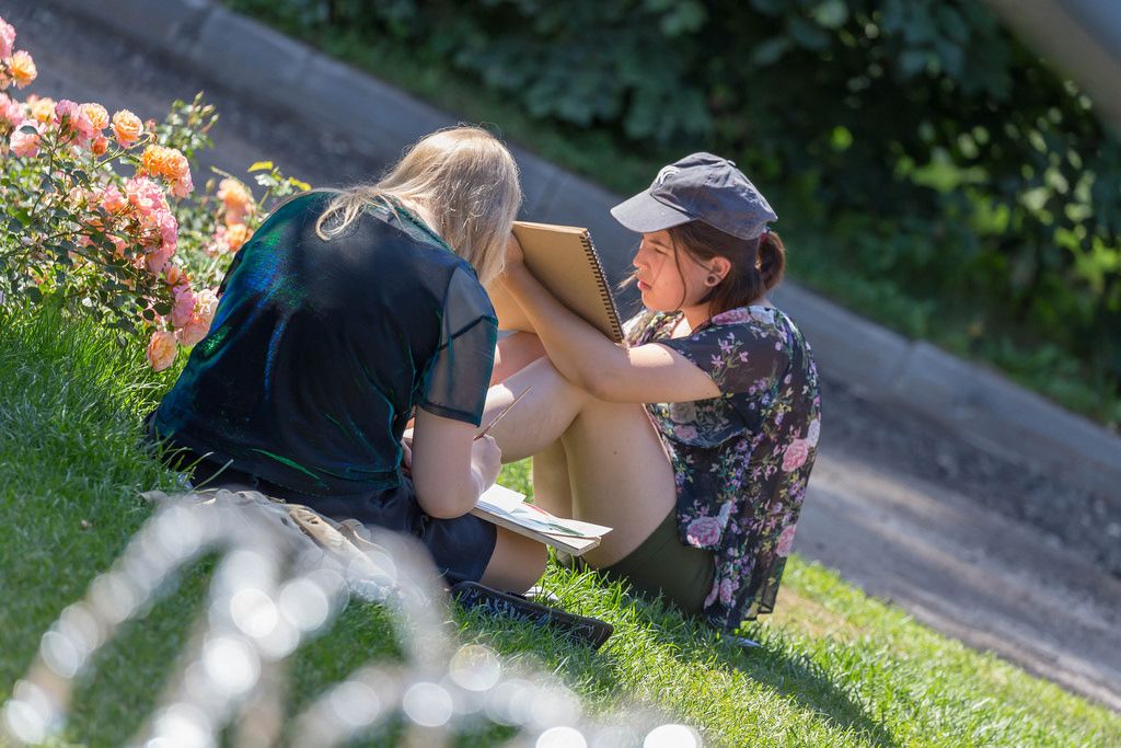 Zwei junge Frauen sitzen auf dem Rasen und malen im Gorki-Park