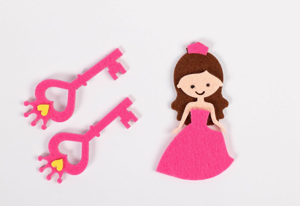 Zwei pinke Schlüssel und Figur einer Prinzessin aus Papier mit rosarotem Kleid vor weißem Hintergrund