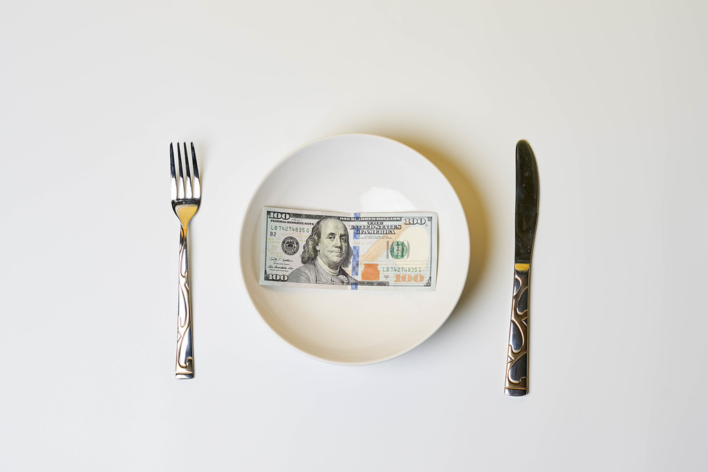 100 dollar banknote on white plate with fork and knife
