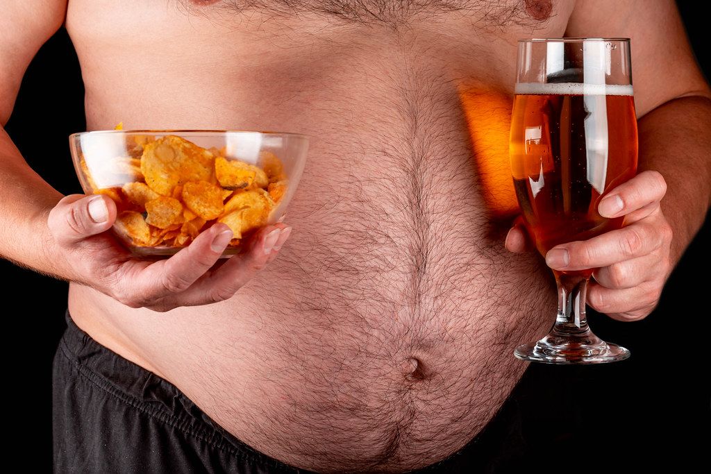A bowl of chips and light beer in men's hands against the background of a large belly