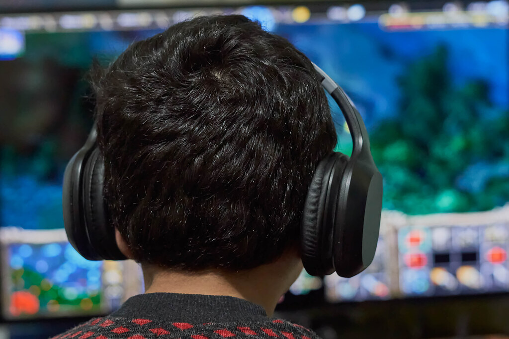 A boy wearing headphones and playing a game console in front of TV