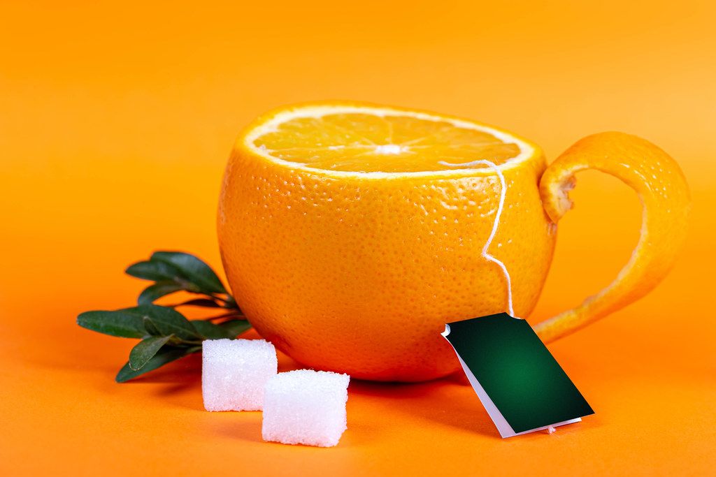 A cup made from fresh tangerine on an orange background with sugar cubes