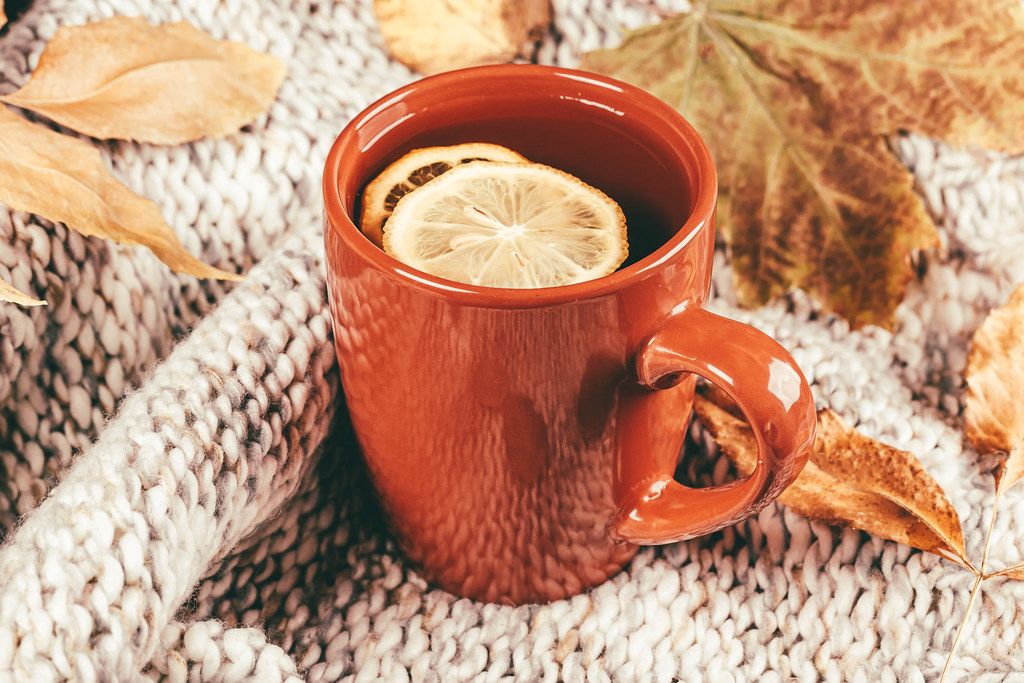 A cup of tea with slices of lemon on a knitted fabric and dry leaves