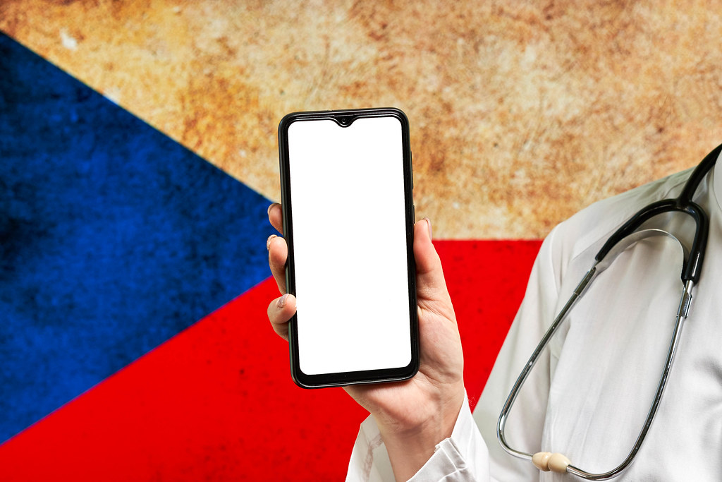 A doctor holds a smartphone with a blank screen over the Czech Republic flag