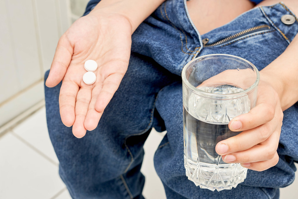 A girl sitting on the toilet, holding a glass of water and medical pills against diarrhea