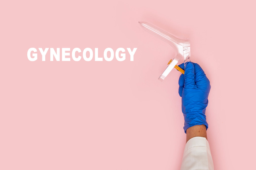 A hand of gynecologist holding vaginal speculum over pink background