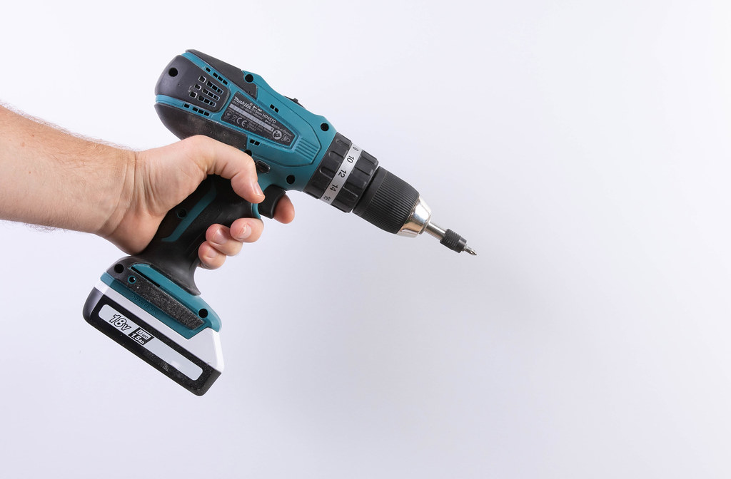 A man holds a cordless drill in his hand on a white background