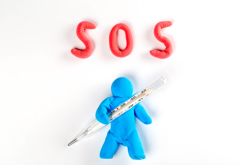 A man made of plasticine with a thermometer in his hands and the inscription SOS on white. Coronavirus concept