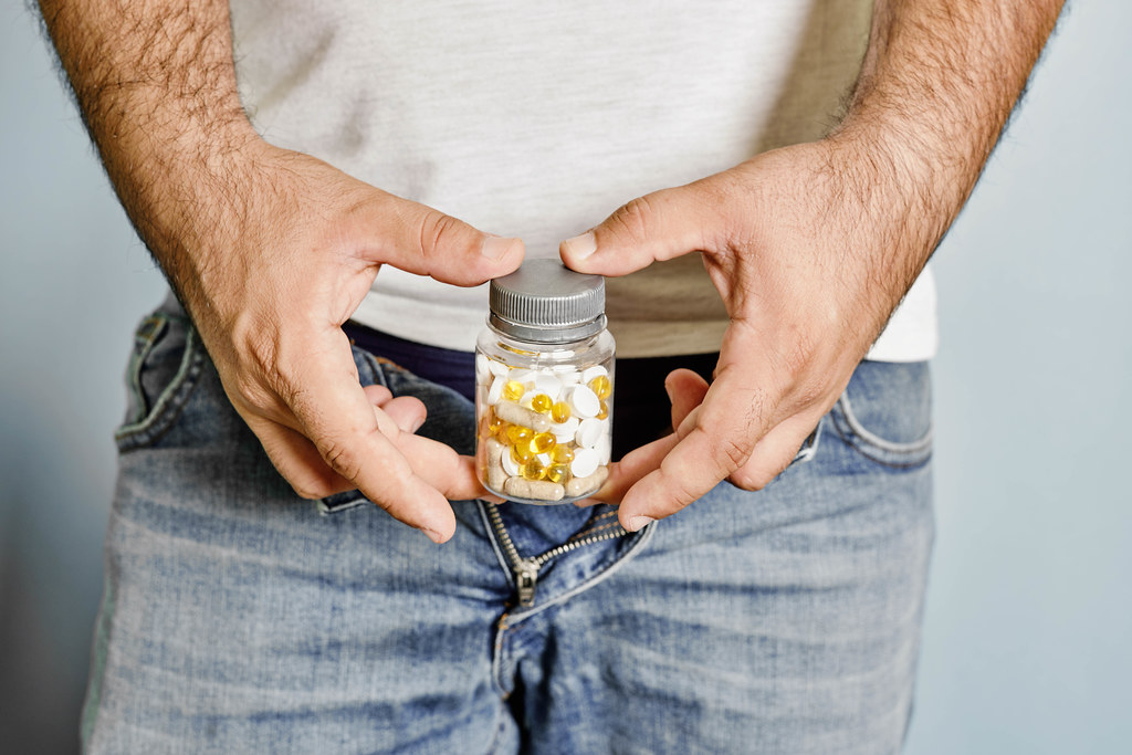 A man with sexual problems holding a container of medical pills near genitals
