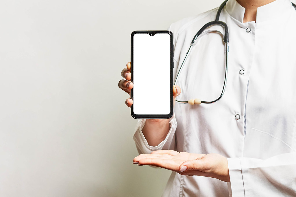 A medical worker holds a smartphone with a blank screen and copy space