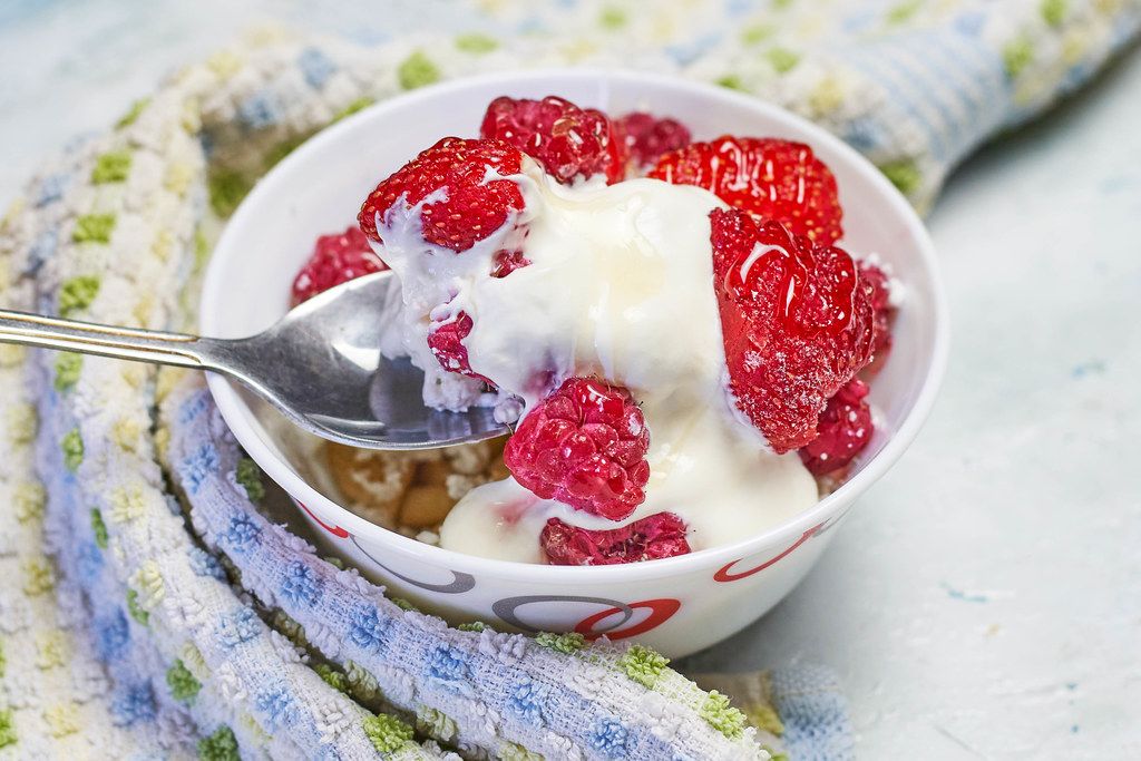 A person eating healthy breakfast yogurt with strawberry and raspberry fruits