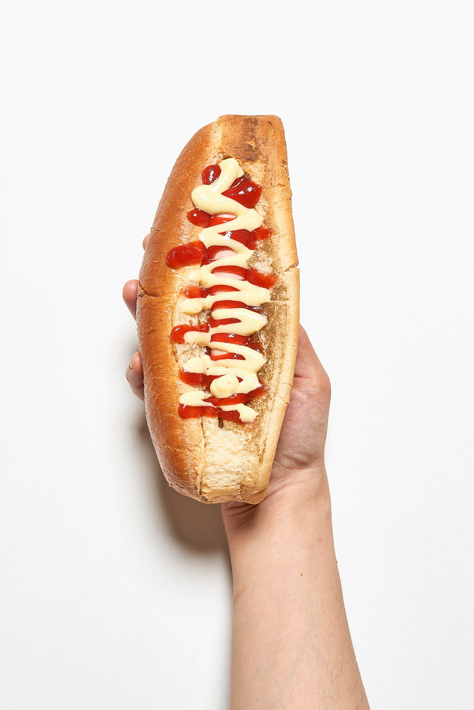 A person hand holding tasty hot dog with mustard and ketchup on white background