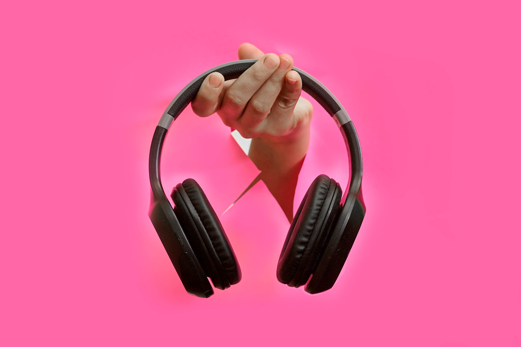 A person hand holding wireless headphones on ripped pink background