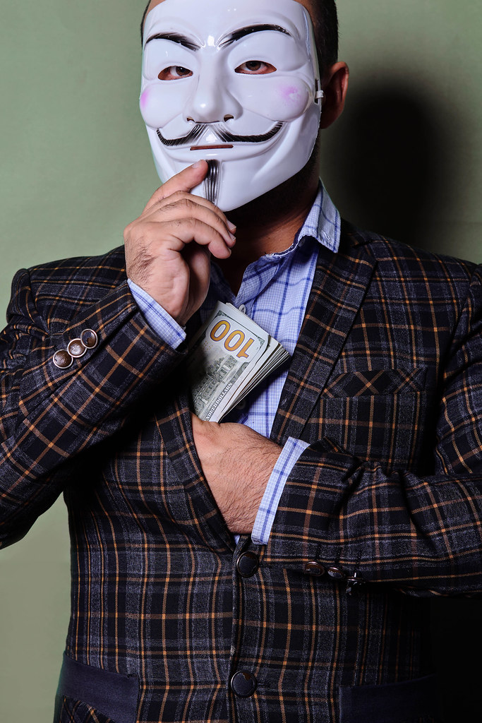 A person hiding his face with anonymous face and putting bribe into pocket - corruption concept