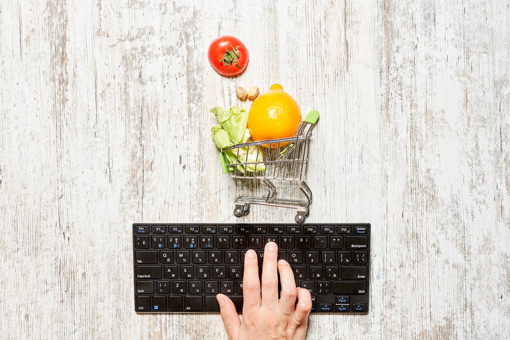 A person ordering grocery online - Keyboard and trolley with fruits