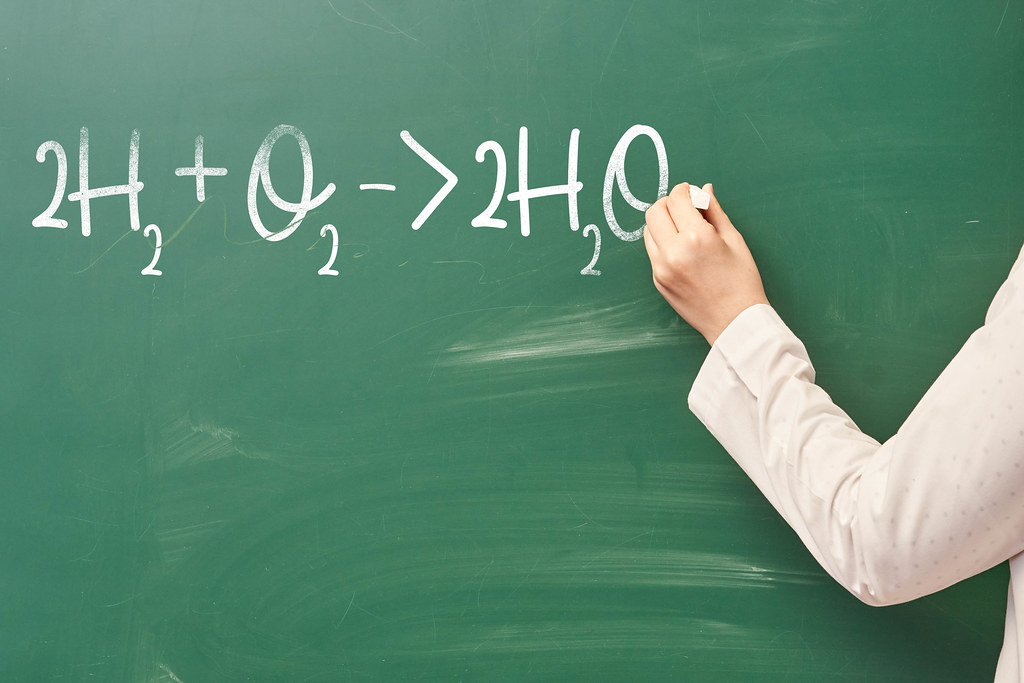 A person writes on a chalkboard chemistry formula