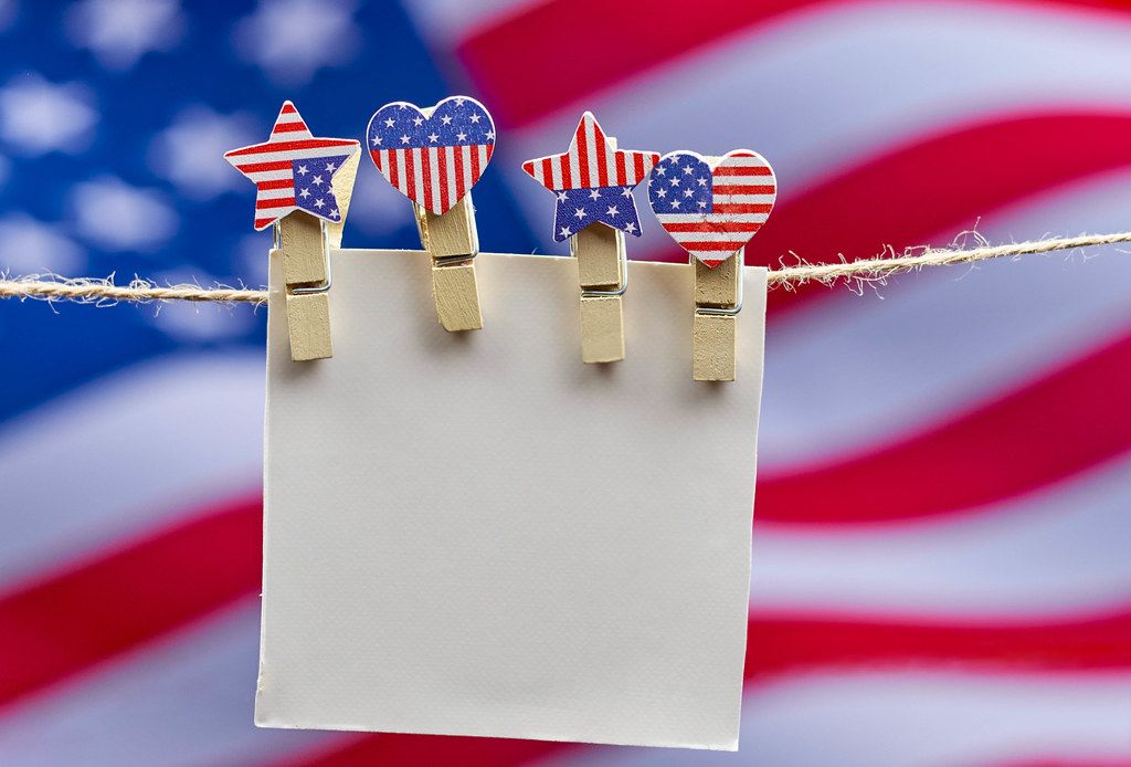 A piece of blank card hanging on the rope with american flag on the background