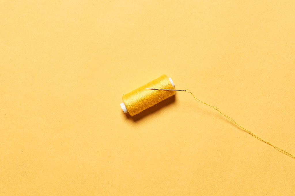 A spool of yellow thread with a needle on yellow background