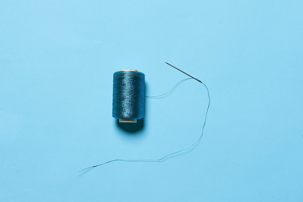 A spool with blue thread and sewing needle on blue background