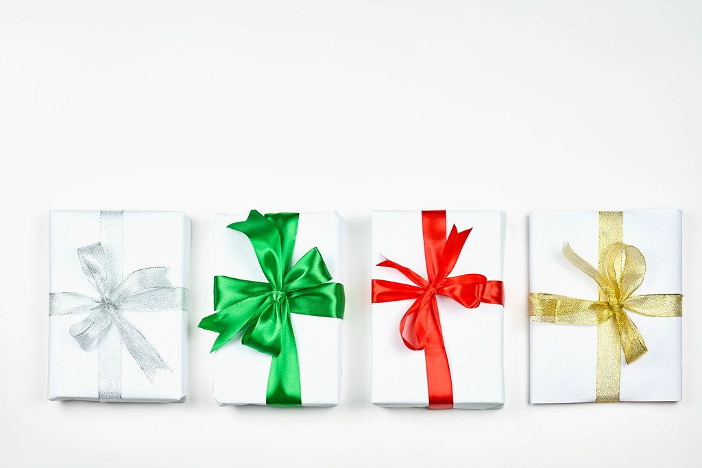 A straight row of four simple paper wrapped Christmas presents with colorful bows
