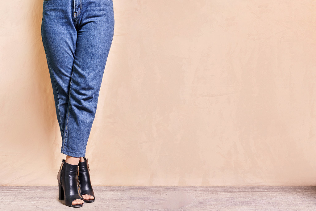 A stylish girl in jeans standing legs crossed over bright background