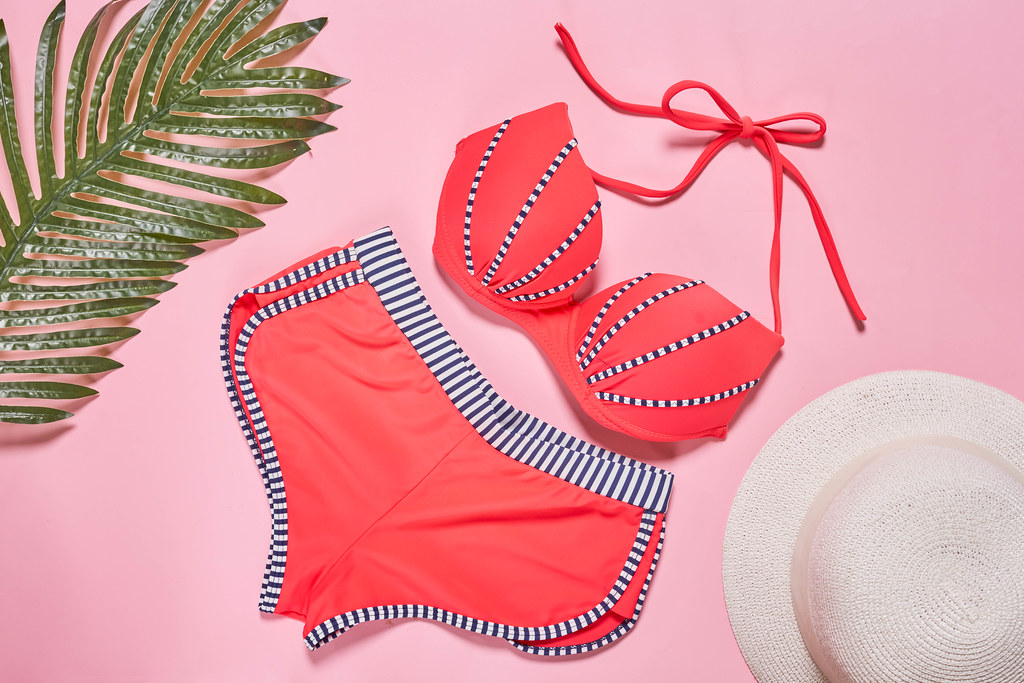 A swimsuit with beach accessories on pink background