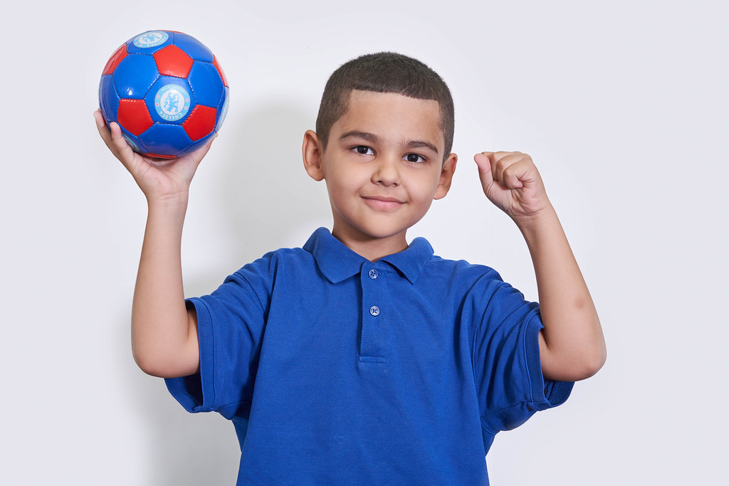 A young boy in blue shirts holding a soccer ball over white background
