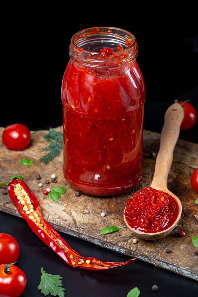 Adjika in a jar and in a wooden spoon, dark background with spices