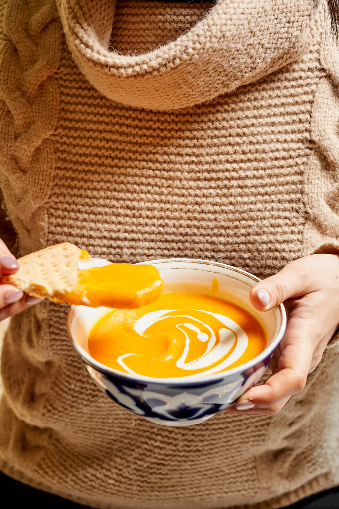 Adult woman eating pumpkin soup in the kitchen