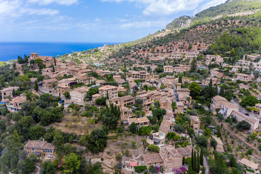 Aerial view of the roofs of Deià amongst orange and olive groves on a hill by the Mediterranean sea