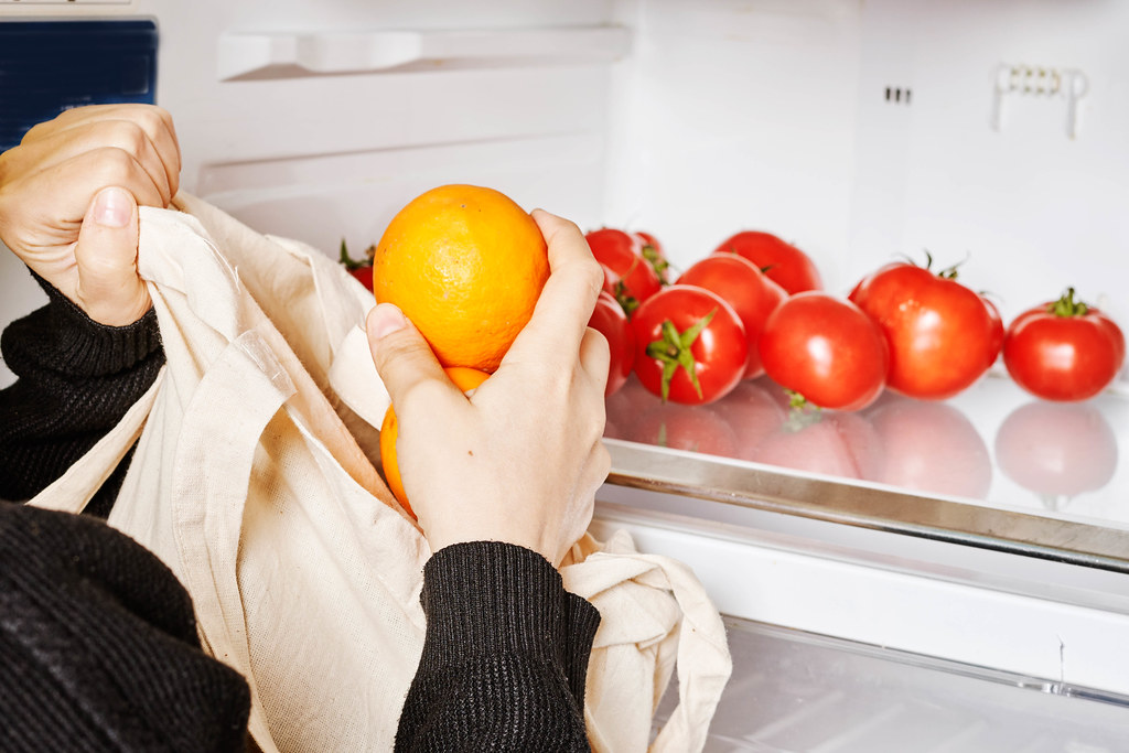 After shopping - woman putting freshly purchased organic vegetables and fruits into the refrigerator