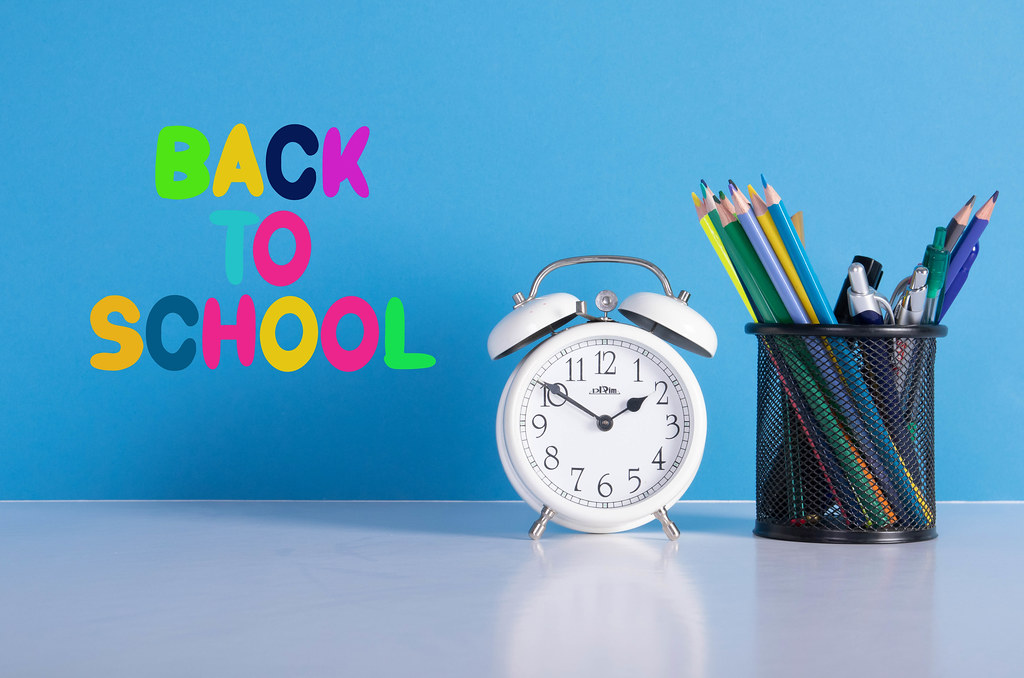 Alarm clock, colored pencils and back to School text on blue background