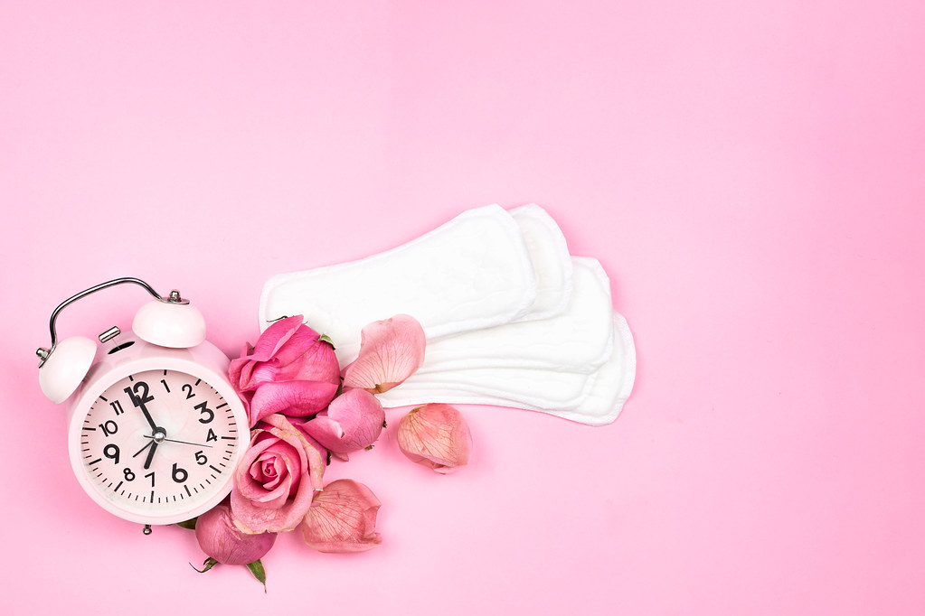 Alarm clock, sanitary pads and beautiful roses on a bright pink background