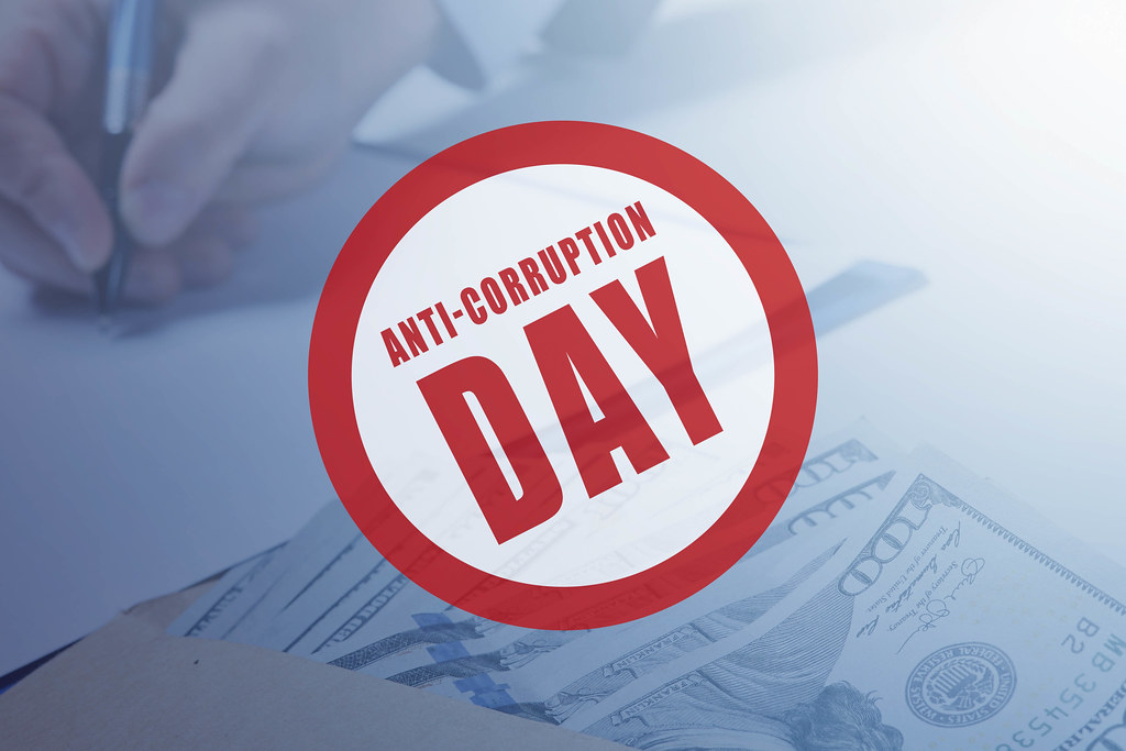 'Anti-corruption day' badge over photo of money and hand signing contract
