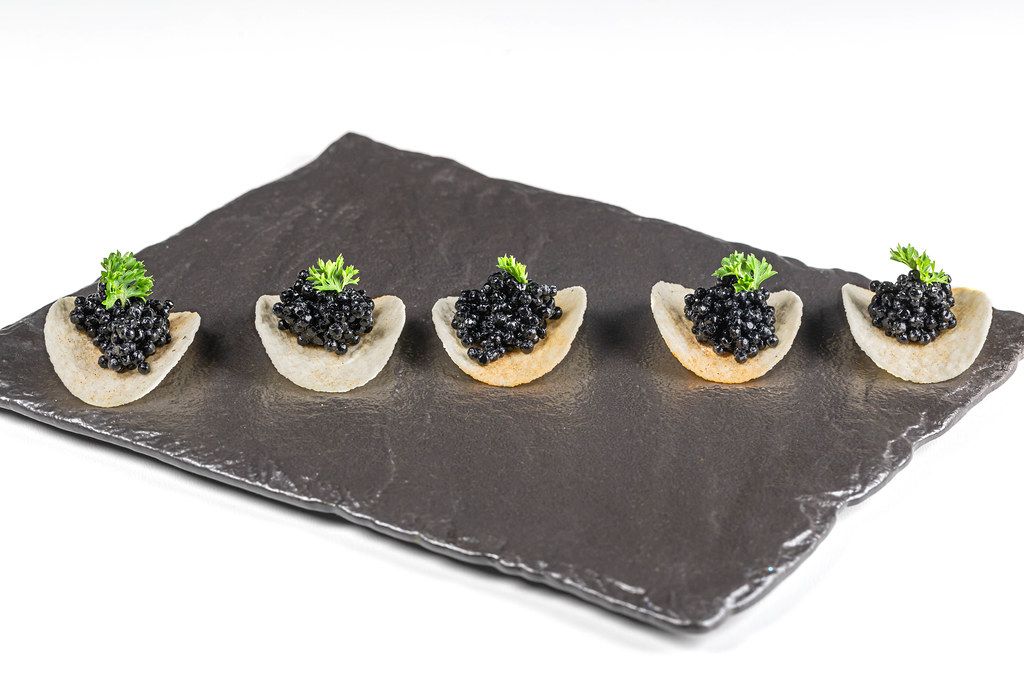 Appetizer of chips with black caviar on black stone tray