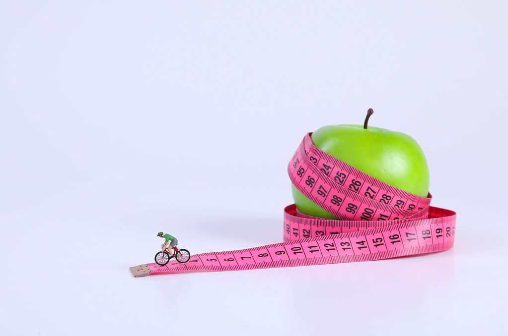 Apple and tape measure with miniature cyclist on white background