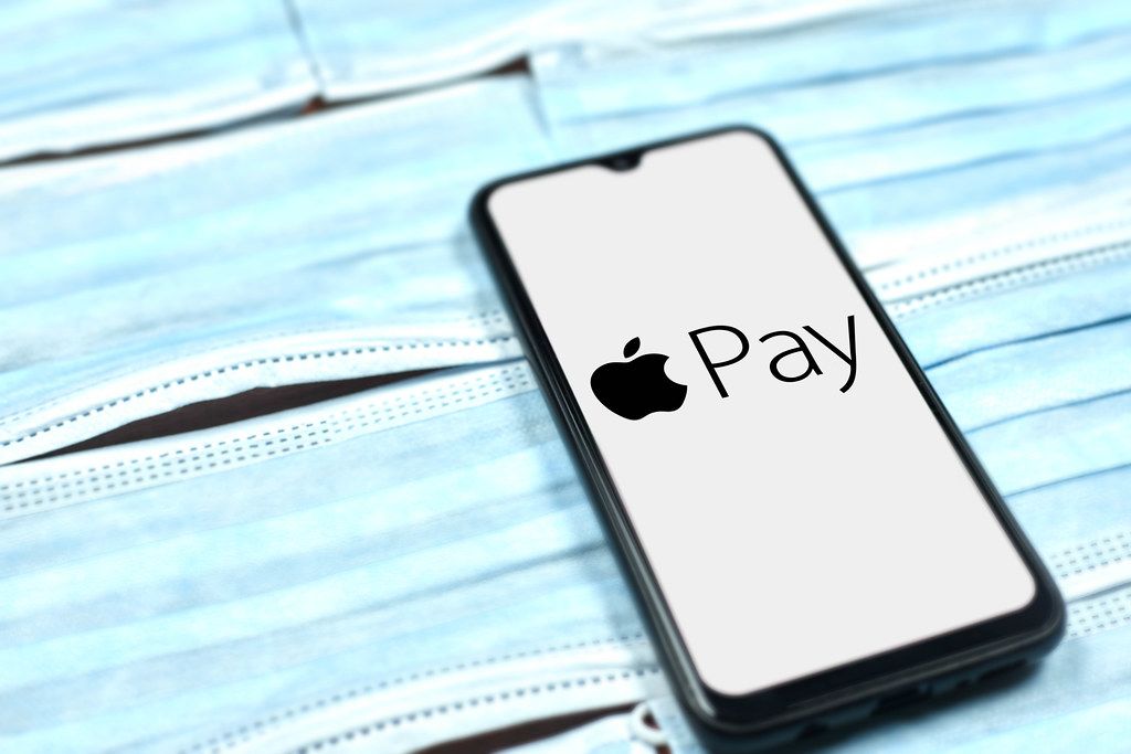 Apple Pay logo on mobile phone over the face masks. Covid-19 effect on company business