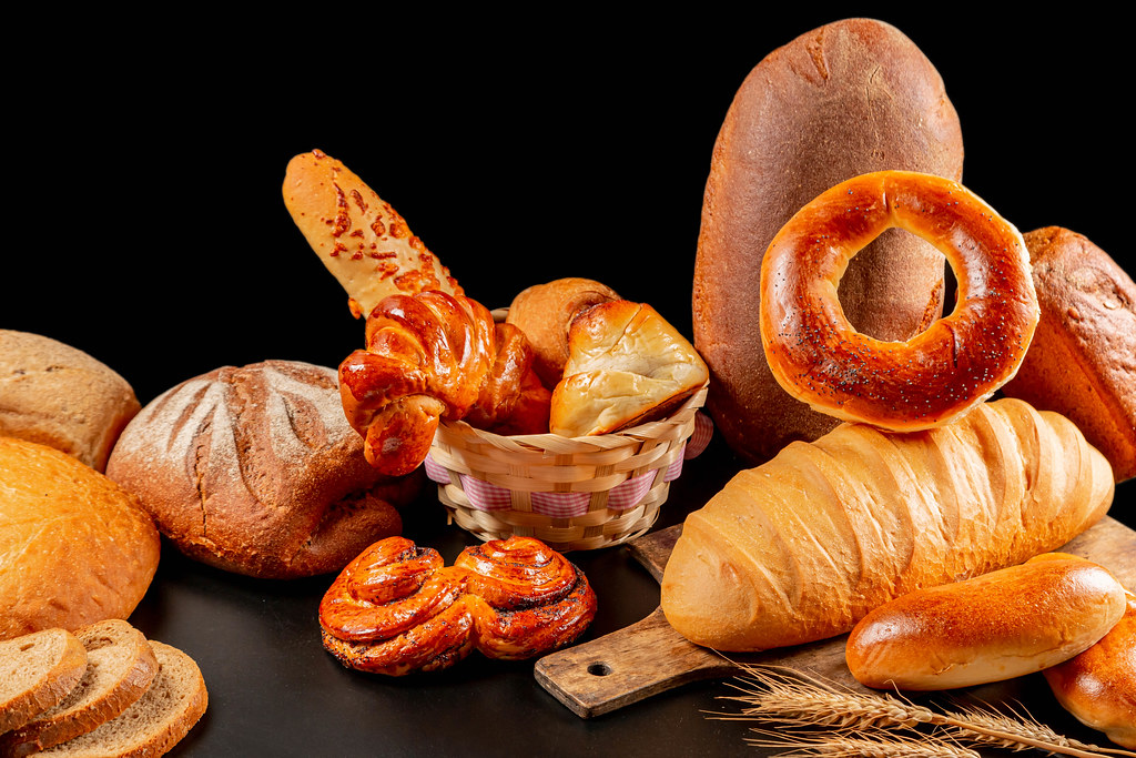 Assortment of fresh assorted baked breads and buns on black background with spikelets