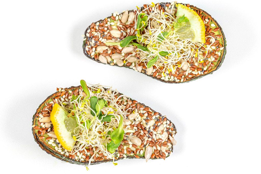 Avocado halves stuffed with microgreens and a mixture of seeds, top view