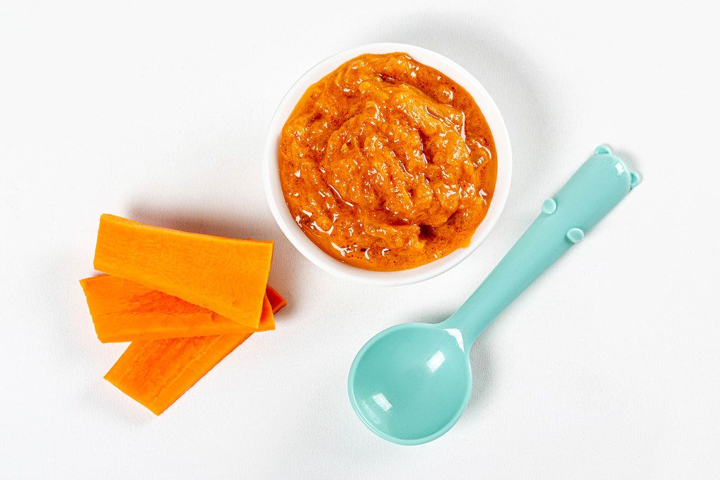 Baby food, bowl of puree with fresh carrots on white background with spoon