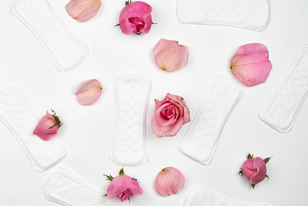 Background with women's hygiene products: loose panty liners, petals and roses on a white background