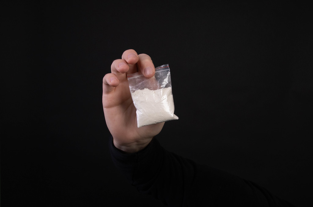 Bag with white narcotic in hand on black background